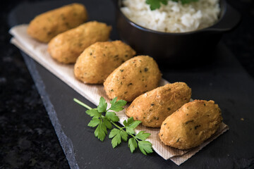 Bolinhos de bacalhau, very famous in Portuguese gastronomy. Fried dumpling, cod dumpling, fish, salted cod fritters, bacalao bunuelos. Codfish cake served with white rice on a dark background.