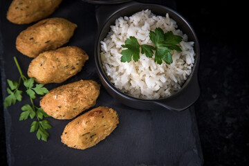 Bolinhos de bacalhau, very famous in Portuguese gastronomy. Fried dumpling, cod dumpling, fish, salted cod fritters, bacalao bunuelos. Codfish cake served with white rice on a dark background.