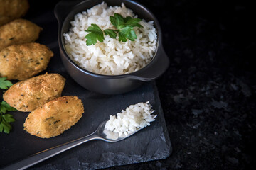 Bolinhos de bacalhau, very famous in Portuguese gastronomy. Fried dumpling, cod dumpling, fish, salted cod fritters, bacalao bunuelos. Codfish cake served with white rice on a dark background.