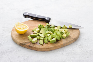 Wooden board with avocado sliced for salad and sprinkled with lemon juice, half a lemon and a knife on a light gray background. Cooking delicious homemade salad