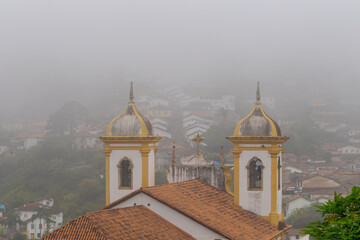 Torre da Igreja Nossa Senhora Mercês e Perdões, centro de Ouro Preto, em manhã com serração de inverno e casario colonial ao fundo