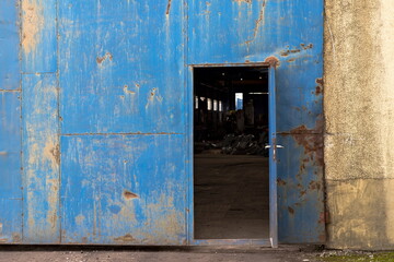 Otwarte drzwi - wmontowane w dużą bramę - do hali przemysłowej . Pordzewiałe pomalowane na niebiesko . W środku widać okna oraz jakieś stalowe elementy konstrukcyjne . - obrazy, fototapety, plakaty