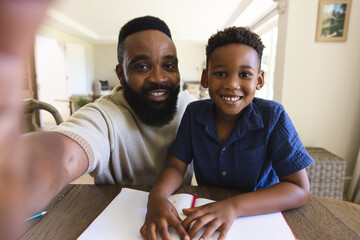Happy african american father and son sitting at table with notebook and having video call