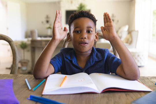 Happy african american boy sitting at table with notebook and having online lesson