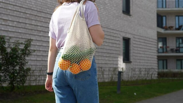 Woman supports ecology and vegetarianism, comes from the store with reusable cloth bags filled with vegetables.