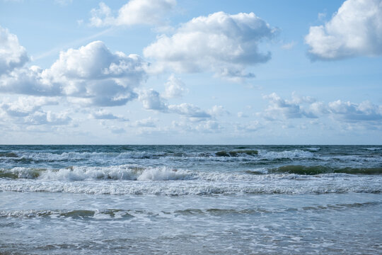 The play of white waves of the sea with clouds in the blue sky.  The rolling sea on a cloudy day.