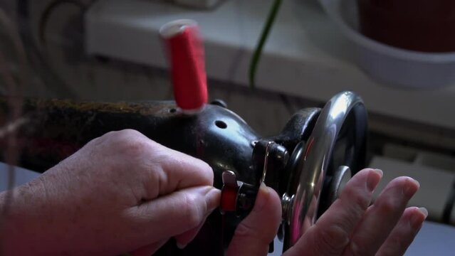 Woman winds a thread for sewing on a typewriter close-up. An elderly woman in glasses sews on an old sewing machine. A seamstress makes a machine-made even seam on a red fabric.