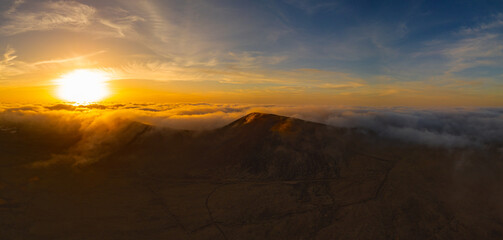 Fototapeta na wymiar Dramatic high level aerial panoramic view of the rare low level cloud, mist or fog over Calderon Hondo volcanic crater at sunset near Corralejo in Fuerteventura Canary Islands Spain
