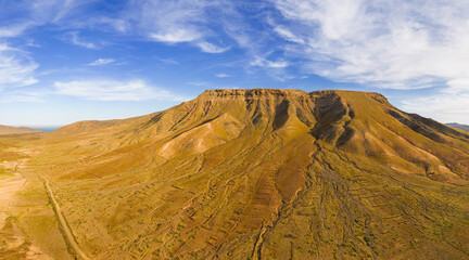 Fototapeta na wymiar Awesome high level aspect panoramic view of the dramatic volcanic mountains and rocky landscape in the late afternoon sun on the island of Fuerteventura in the Canary Islands Spain
