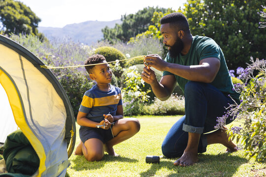 Happy african american father and son pitching tent in garden - Powered by Adobe