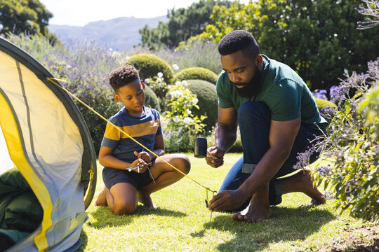 Happy african american father and son pitching tent in garden - Powered by Adobe