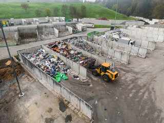 Handling construction waste on the landfill site, skid steer loader scooping and dumping dusty...