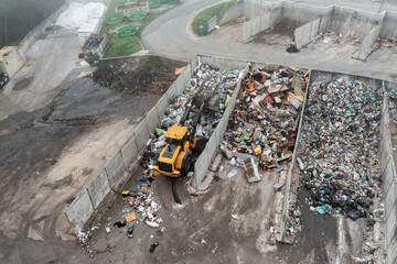 Yellow wheel loader, with lifted scrap grapple, moving along the recycling center area in process...