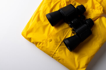Close up of yellow rainproof coat and binoculars on white background with copy space