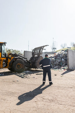 Man In A Blue Working Suit Looking At Garbage Near Landfill Skid Steer Loader