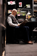 Senior private detective reading legal documents in arhive room, working overhours at criminal...
