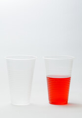 2 plastic cups, one full of red liquid, the other empty, vertical photo on white background