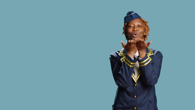 Female aircrew member sending air kisses on camera, acting flirty and cute in studio. Young stewaress dressed in uniform showing romantic sweet gesture, doing kissy face. Aviation job.
