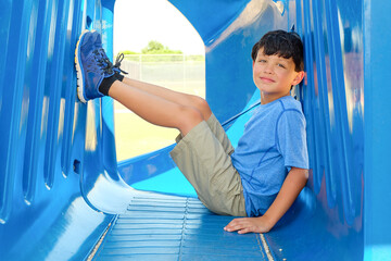 Smiling young boy sitting on playground equipment outside on a sunny day