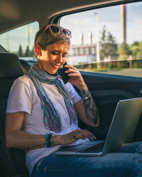 One Mature Woman Caucasian Female Sitting On The Back Seat Of The Car Working On Laptop Computer Make A Phone Call Talk In Summer Day With Short Gray Hair Modern On Road Wearing Casual Copy Space