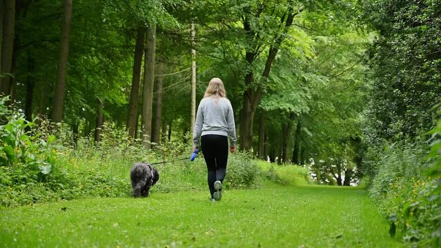 Blonde woman walks black labradoodle dog on track
