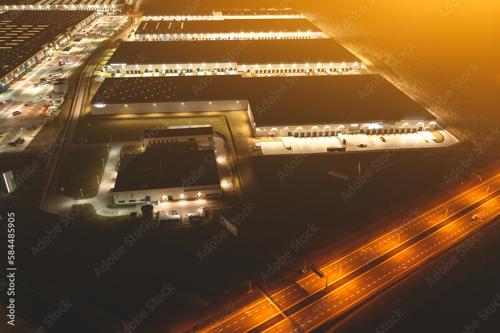 Wall mural many warehouses in an industrial area, aerial view of brightly lit logistics warehouses at night, tr