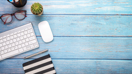 Wooden desk workplace with keyboard, mouse, pen, eyeglass and notebook, Top view flat lay with copy space.