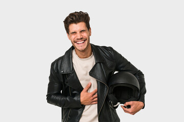Young caucasian man holding a motrbike black helmet isolated laughing and having fun.