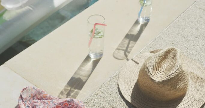Straw hat, drinks and inflatables in swimming pool in garden on sunny day
