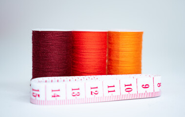 takes about three spools of orange thread of different shades and a white tape measure with red numbers on a white background.