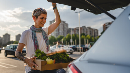One woman mature caucasian female stand at the back trunk of her car on the parking lot of the...