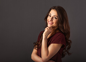 Beautiful happy smiling thinking  business woman have an idea in dark red blouse with curly healthy brown hairstyle on grey background with empty copy space for text. Closeup