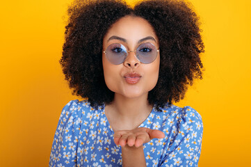 Pretty, positive trendy african american curly haired woman with blue glasses, wearing blue summer...