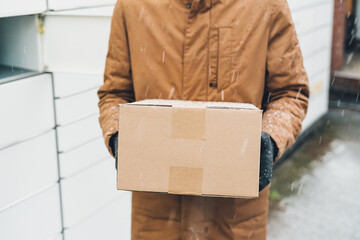 A man with a box in his hands near the self-service mail terminal. Parcel delivery machine. Person...