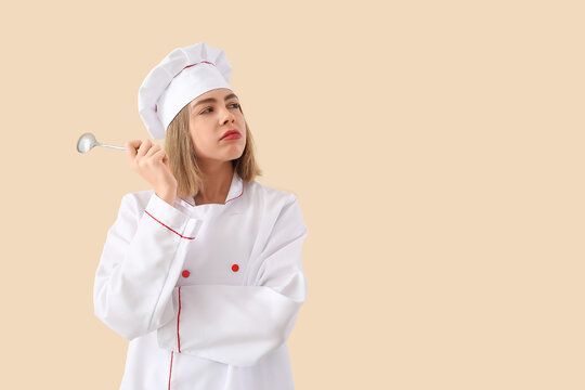Thoughtful female chef with tablespoon on beige background