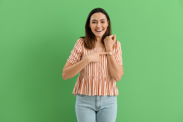 Young woman pointing at stylish wristwatch on green background