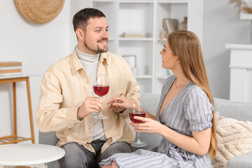 Young couple with glasses of wine sitting on sofa at home