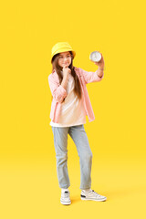 Thoughtful little girl with alarm clock on yellow background