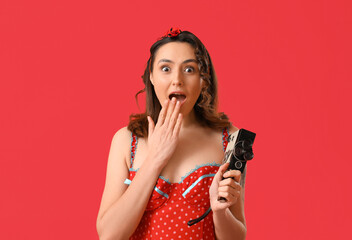 Surprised young pin-up woman with retro video camera on red background