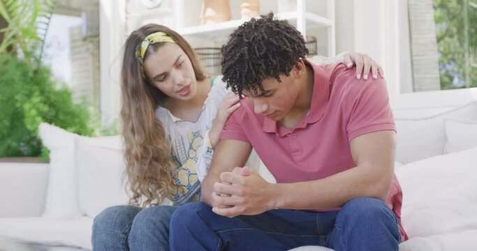 Sad biracial couple spending time at home together sitting on couch and cheering