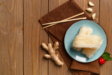 Plate with raw rice noodles and chopsticks on wooden background