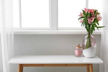 Fototapeta na wymiar Vase with alstroemeria flowers and candle on table near window