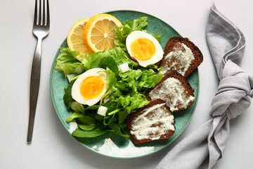 Plate of delicious salad with boiled eggs and cream cheese sandwiches on grey background
