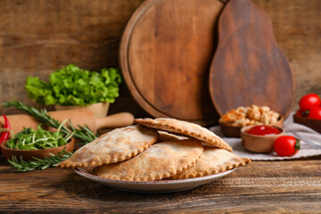 Plate with baked meat empanadas, herbs and sauce on wooden table