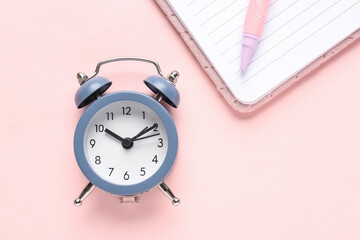 Alarm clock, notebook and pen on pink background