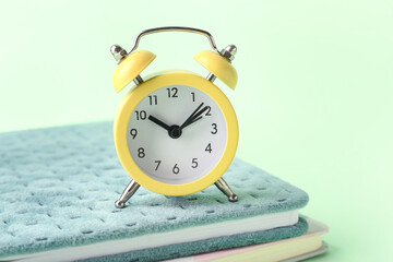 Notebooks and alarm clock on color background, closeup