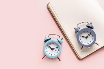 Alarm clocks and notebook on pink background