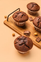 Wooden board with tasty chocolate cupcakes on beige background