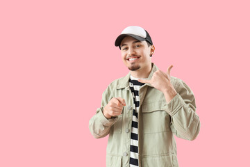 Cool young man showing "call me" gesture and pointing at viewer on pink background