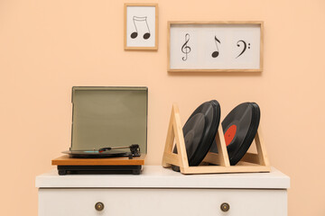 Vinyl records and player on white wooden drawer dresser near beige wall